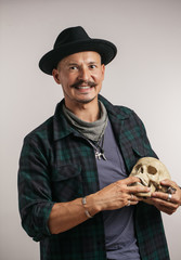 Stylish European man with mustache wearing hat and holding scull while posing indoors, with copy...