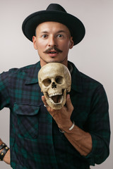 Stylish European man with mustache wearing hat and holding scull while posing indoors, with copy space for your text or promotional content