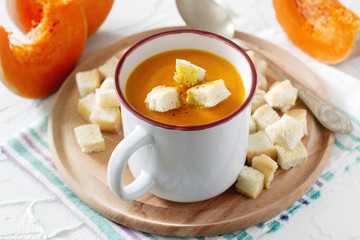 Delicate vegetable cream soup with pumpkin and croutons and slices of pumpkin on a light background.
