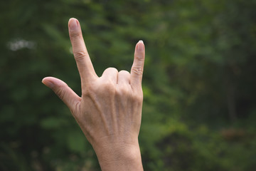 Closeup hand of person doing symbol for i love you in garden green nature background.