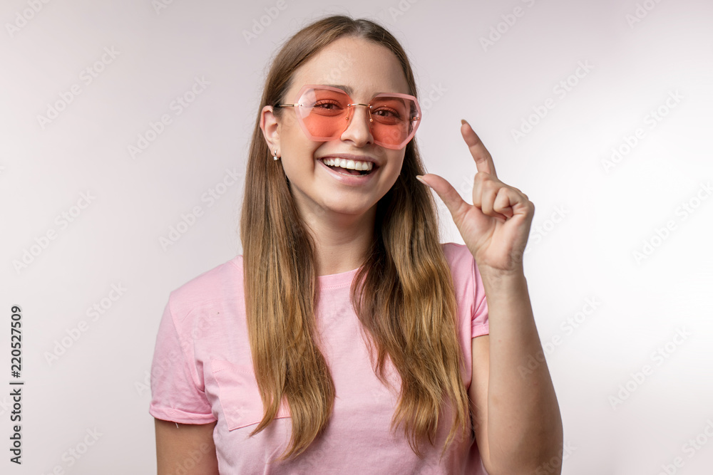 Wall mural cheerful beautiful woman dressed casually showing something tiny with fingers, isolated overwhite background.size, gesture concepts