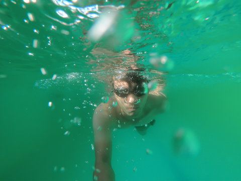 Young man dive underwater in the ocean, 
man wear a SWIMMING GOGGLES under the green water with a bubbles.
summer vacation activity, swimming in the warm tropical sea.
