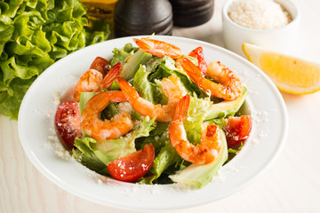 Fresh Caesar shrimp salad with delicious prawns, ruccola, spinach, cabbage, arugula, egg, parmesan and cherry tomato on wooden background. Oil, salt and pepper. Healthy and diet food concept.