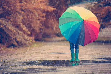 Child walking in wellies in puddle on rainy weather. Boy holding colourful umbrella under rain in summer © candy1812