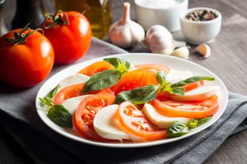 Photo of Caprese Salad with tomatoes, basil, mozzarella, olives and olive oil on wooden background. Italian traditional caprese salad ingredients. Mediterranean, organic and natural food concept.