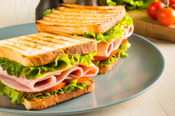 Close-up of two sandwiches with bacon, salami, prosciutto and fresh vegetables on rustic wooden cutting board. Club sandwich concept.