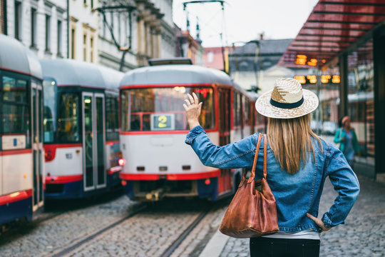 Woman is wearing jeans jacket and a straw hat, she is waving on leaving tram in the city. Say goodbay to leaving person