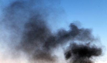 Obraz na płótnie Canvas black smoke pillar against the blue sky background.