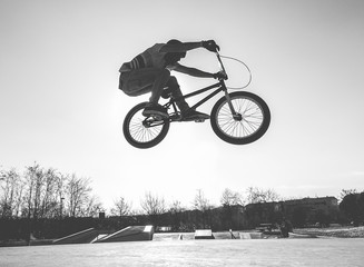 Bmx biker jumping in city skate park outdoor - Young trendy man performing skills and tricks with...