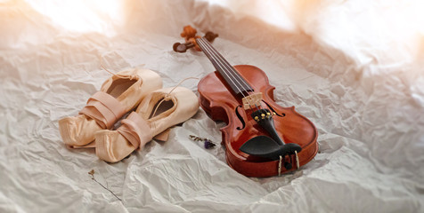 The ballet shoes and violin put on background,warm light tone,blurry light around.