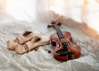 The wooden violin put beside ballet shoes,warm light tone,blurry light around
