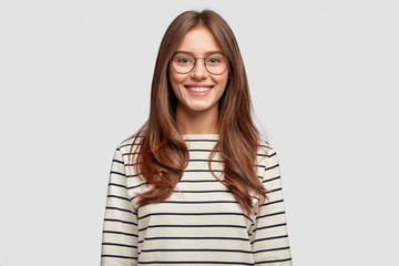 Indoor shot of attractive European schoolgirl has toothy smile, dressed in striped sweater,...