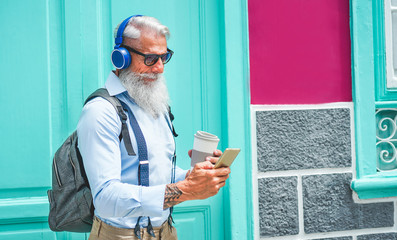 Trendy senior man using music smartphone app and drinking coffee in downtown center outdoor