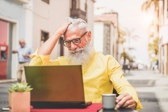 Trendy bearded senior using laptop in bar cafeteria outdoor