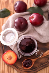 Composition with tasty plum jam in jar on wooden board