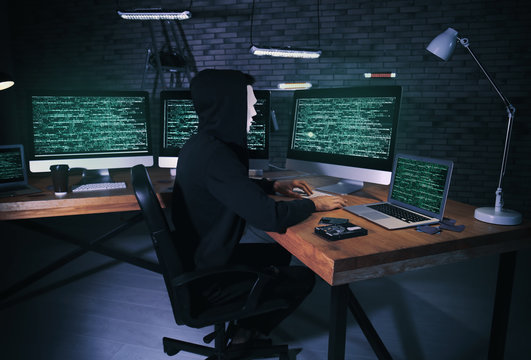 Masked hacker using computer in dark room. Threat of cyber attack