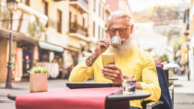 Happy trendy man drinking coffee and using smartphone in bar cafeteria outdoor