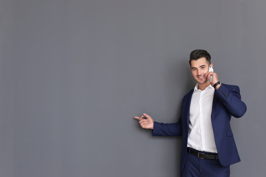 Handsome young man talking on phone against grey background. Space for text