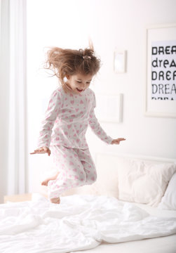 Cute little girl jumping on bed with soft pillows at home