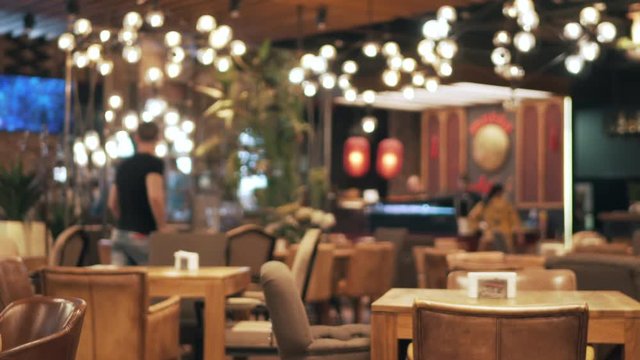 Blurred picture of the interior of a large beautiful restaurant with bright lighting. The waitress comes to the table and gives the visitors a menu and goes for drinks. Defocused restaurant