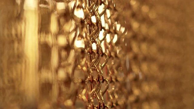Slow, smooth movement of long gold chains. Uniform swing. Gold background for relaxation. Meditation. Relax. Texture for soothing. Glitter. Vertical picture. Blurred