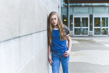 Sad teenage girl leaning against brick wall of a school.