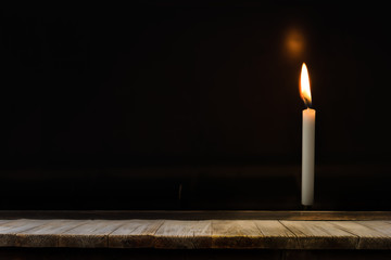 Wooden table in front of light candle burning brightly in the black background, can used for...