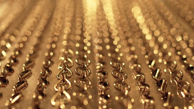 Slow, smooth movement of long gold chains. Uniform swing. Gold background for relaxation. Meditation. Relax. Texture for soothing. Glitter. View from bottom to top. Blurred