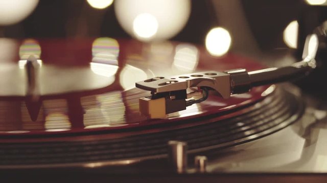 A slide turntable vinyl record player. The vinyl record on DJ turntable record player close up. The stylus smoothly with a needle onto a rotating red vinyl plate. Included gramophone and torque plate 