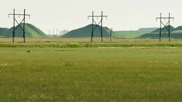 High Voltage Electric Transmission Tower Energy Pylon. Green hills of mining waste in the background.