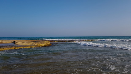 A rocky beach with sea waves and a clear sky on a sunny day.