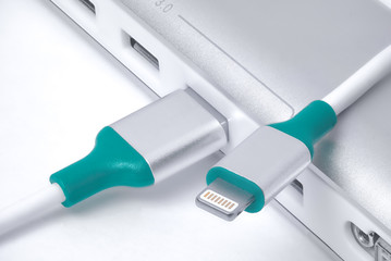 usb speed cable for phones Lightning . cable connectors and silver with a plastic colored insert. on white background with laptop beside white cable.