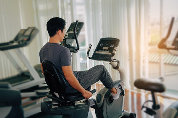 muscular young asian man exercising his legs cardio training on bicycle in fitness gym for good...
