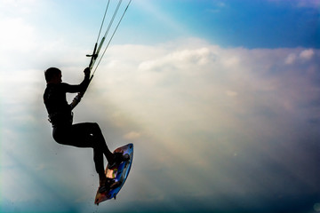 Kite surfer in a stunt silhouetted against a blue sky with sunstreaks