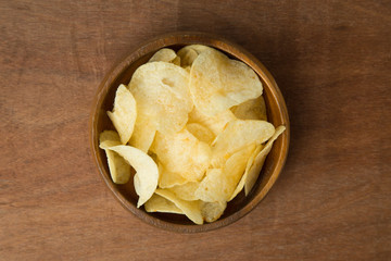 Top view of potato chips in wooden bowl on wooden background.