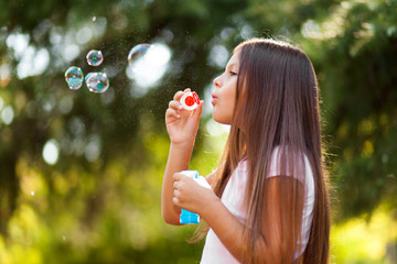 Children girl blowing soap bubbles in outdoor forest