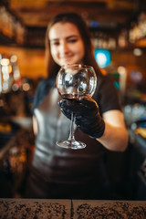 Female bartender in apron holds out a glass