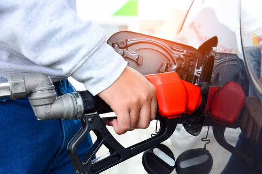 man holding red fuelling nozzle and pumping gasoline fuel fill in car at gas station, car fuels or transportation concept