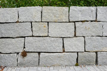 Moderne Stütz- und Abgrenzungsmauer aus großen roh zugehauenen Granitblöcken an einem Auto-Parkplatz