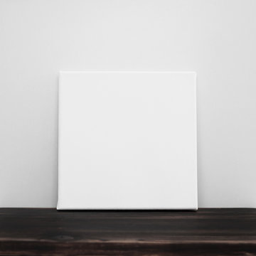 White square canvas. Gray wall and wooden floor background. Poster template.