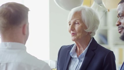 Medium shot of friendly elderly woman saying kind words to colleagues during retirement party in office