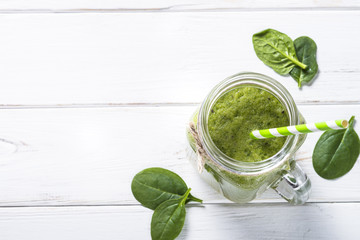 Green smoothie and ingredients on white wooden table.