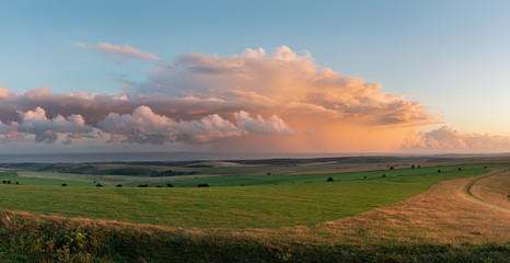 Stunning large panorama of Summer sunset landscape image of South Downs National Park in English countryside with stunning dramatic storm clouds out at sea in the distance