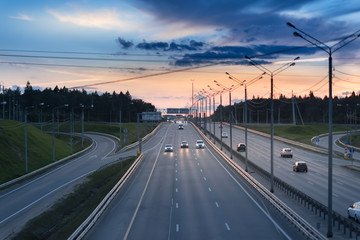 Fototapeta premium Car and light on the road. Sunset on the evening highway with metal safety barrier