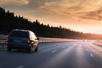Fototapeta premium Car and light on the road. Sunset on the evening highway with metal safety barrier