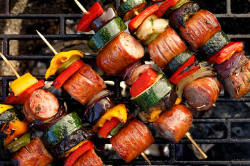 Grilled skewers of meat, sausages and various vegetables on a grill plate, outdoors, top view....
