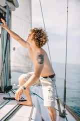 Sailor or tourist with haked torso and tattooed arm working on ship or sailing boat, preparing...