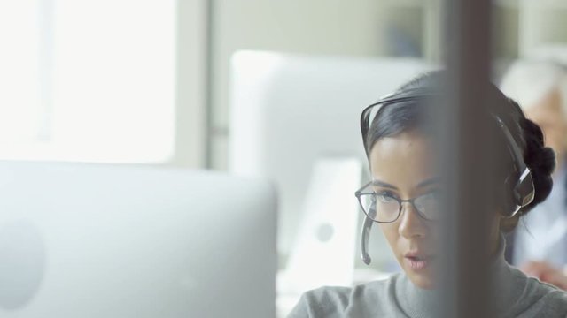 Tilt Down Shot Of Young Mixed Race Woman Using Desktop Computer And Headset For Work In Customer Service