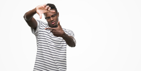 Young african american man wearing glasses and navy t-shirt smiling making frame with hands and fingers with happy face. Creativity and photography concept.