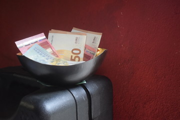 Schale mit Geld steht auf Geldkoffer vor roter Wand
